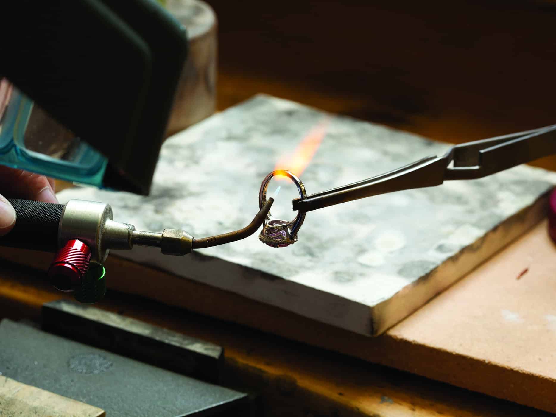 a ring being held in tweezers while a jeweler is using a torch to repair it